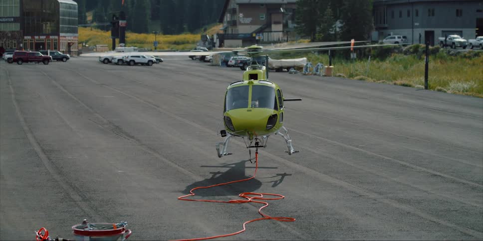 A helicopter with a long rope attached to it lands on a road