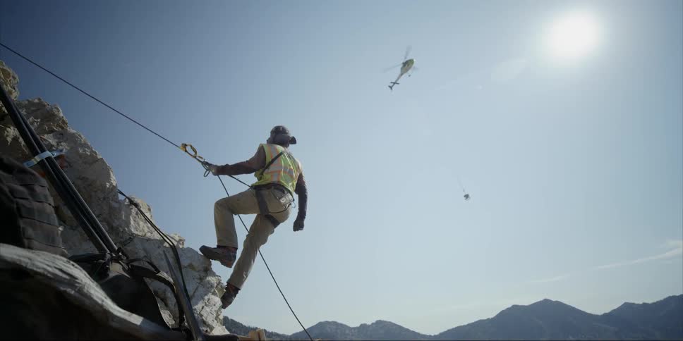 A rock climber watches a helicopter fly overhead in the mountains