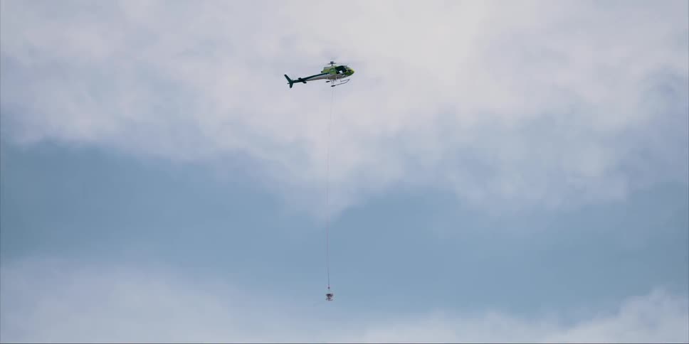 A helicopter flies high in the cloudy sky