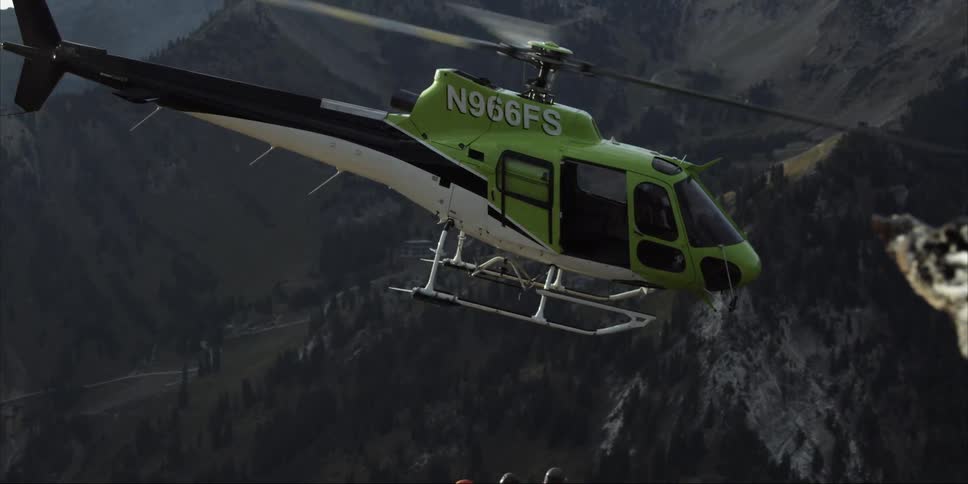 Workers crouch on a mountainside as a helicopter lifts away from them