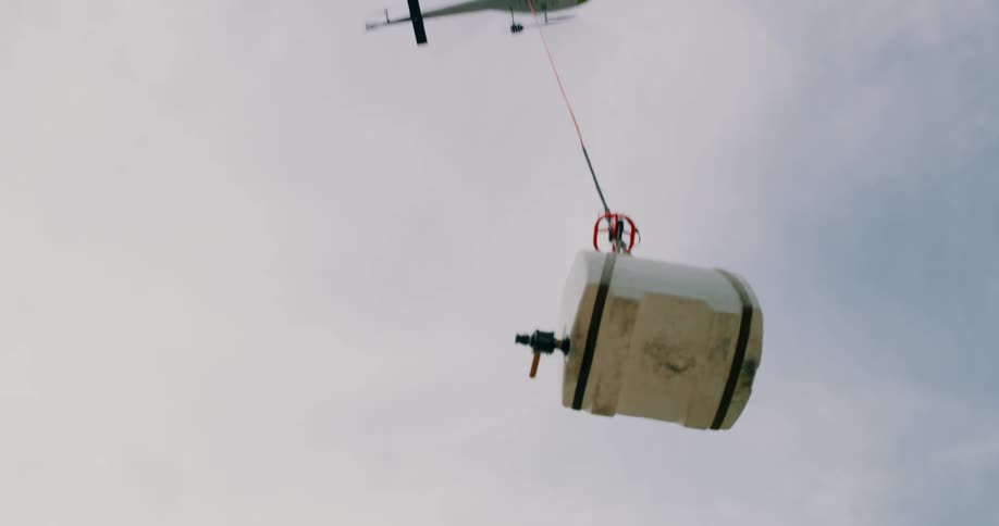 A helicopter lifts a container into the air with a cable
