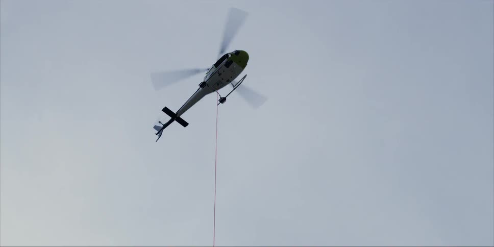 A helicopter is hovering with a rope attached to the bottom of it