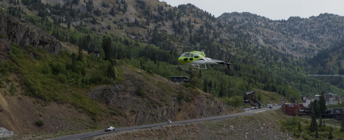 A helicopter is lowering down near a road in a mountain valley during the day
