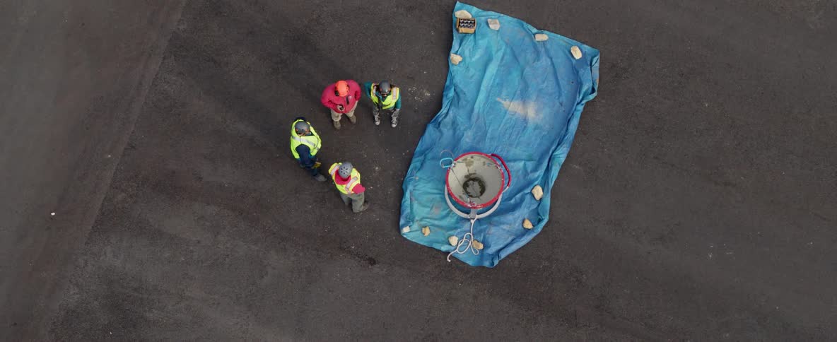 Four men standing near a blue tarp and metal bin
