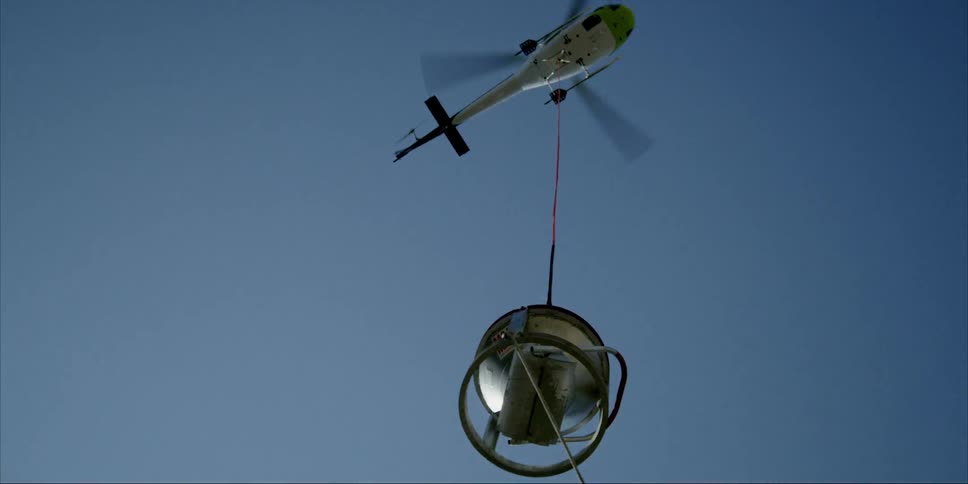 A helicopter raises up a metal bin into the sky