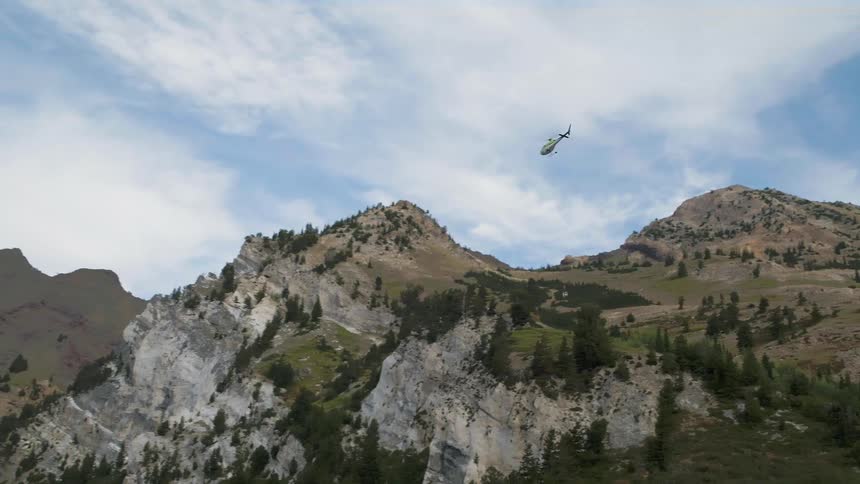 Helicopter carrying a large bin by rope over mountains