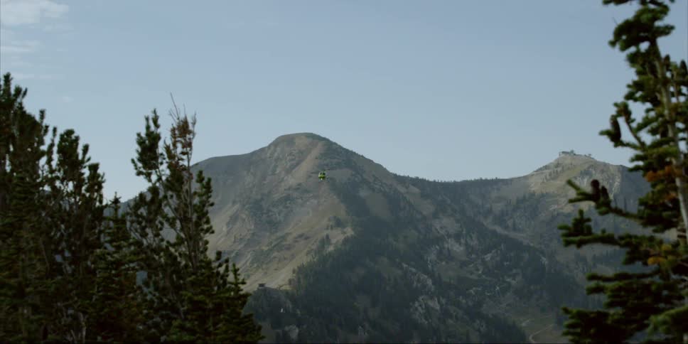 A helicopter is rising into the air above and flying above a mountain range in daylight