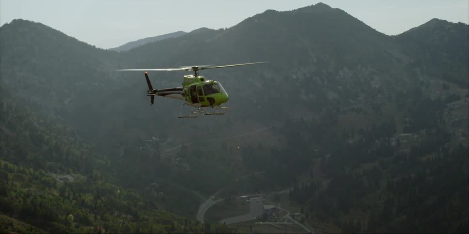 A helicopter is flying above a mountain range in daylight