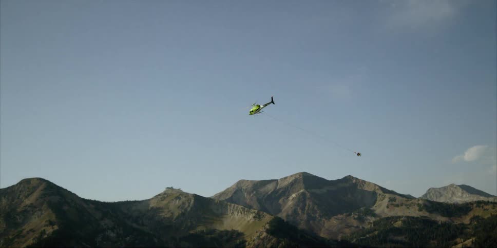 Helicopter carrying a large bin by rope over mountains