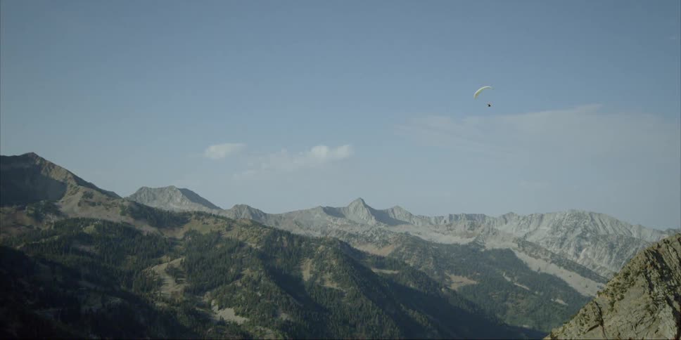 A paraglider is soaring over mountains on a sunny day