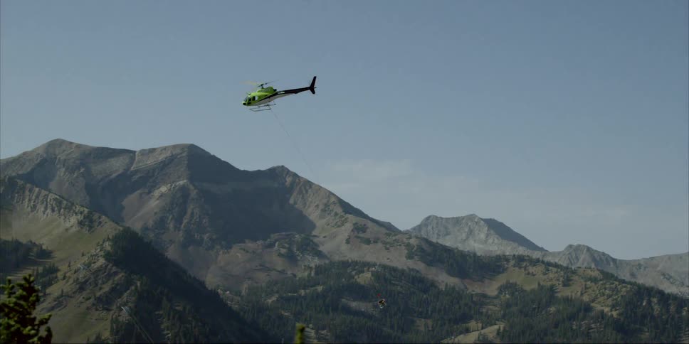 Helicopter carrying a large bin by rope over mountains