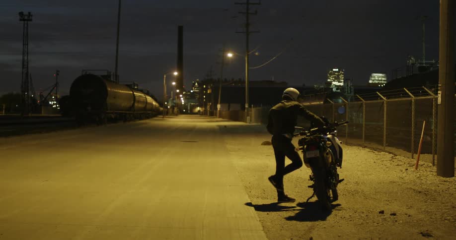 Man parks a motorcycle on a town street at night