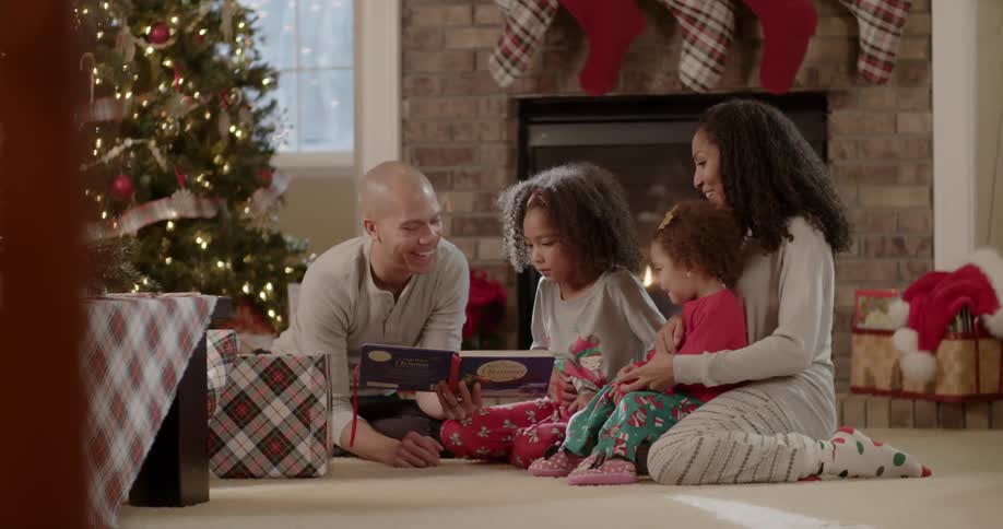 A mother and father read to their two young kids near the christmas tree