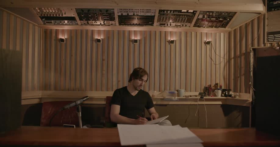A man is writing in a notebook as he sits in a music recording studio