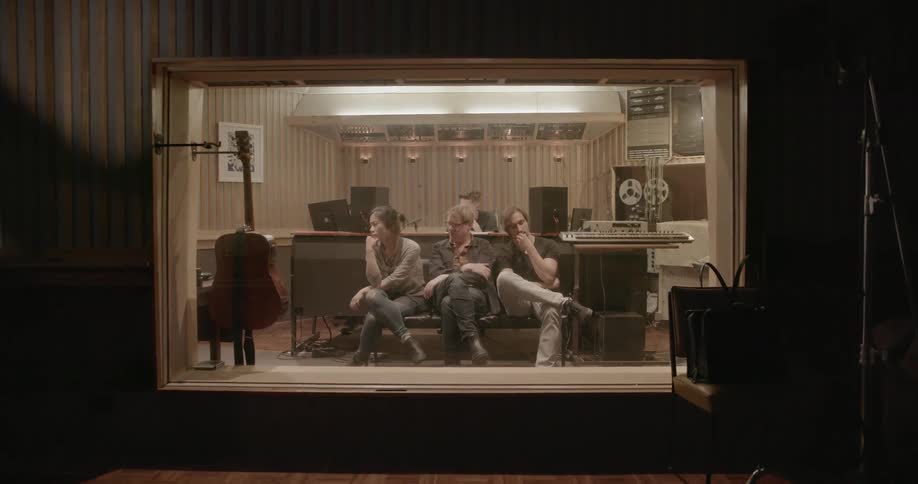 Three people are sitting and listening in a music recording studio