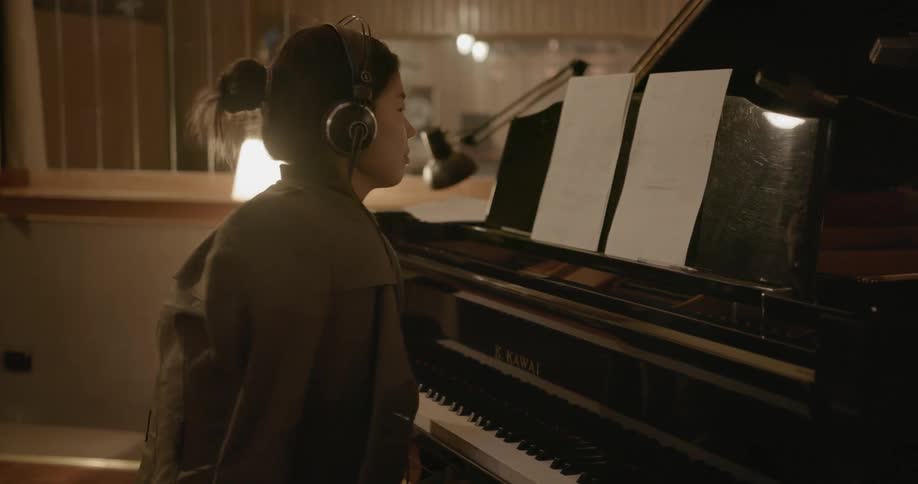 A lady is reading sheet music in front of a piano