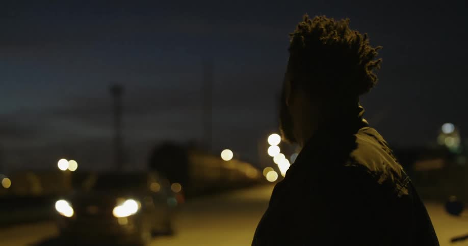 A man rubs his hands together while waiting outside at night