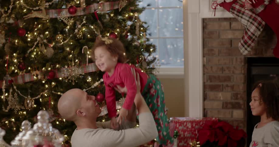 Man tosses a young girl into the air next to a christmas tree
