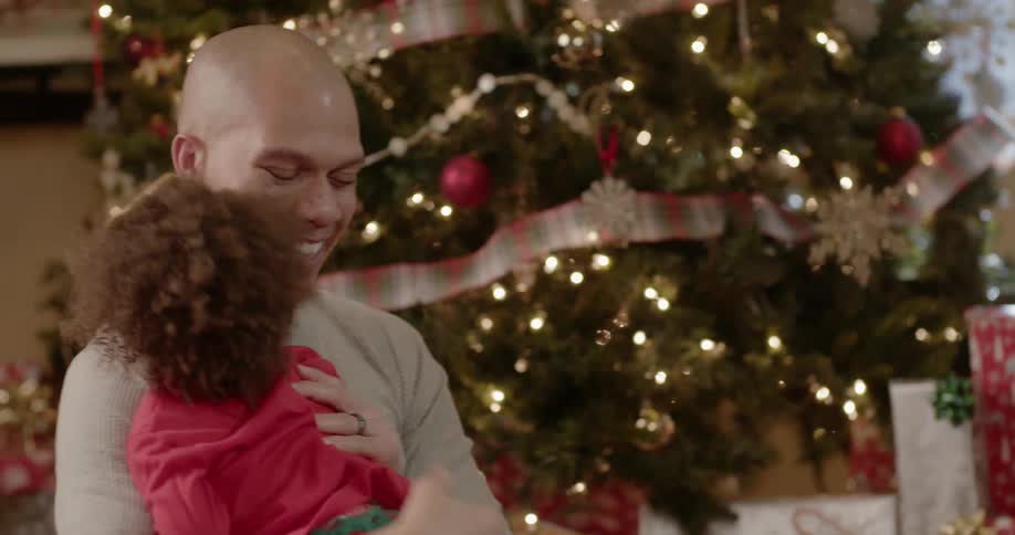 A girl jumps into her dad's arms near the christmas tree