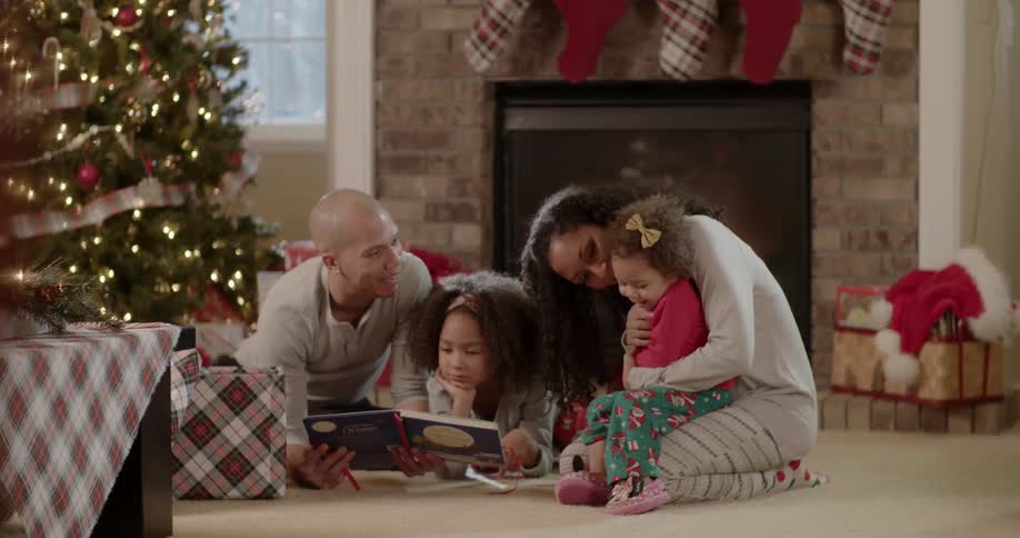 A family a reading a book on a living room floor at christmas time