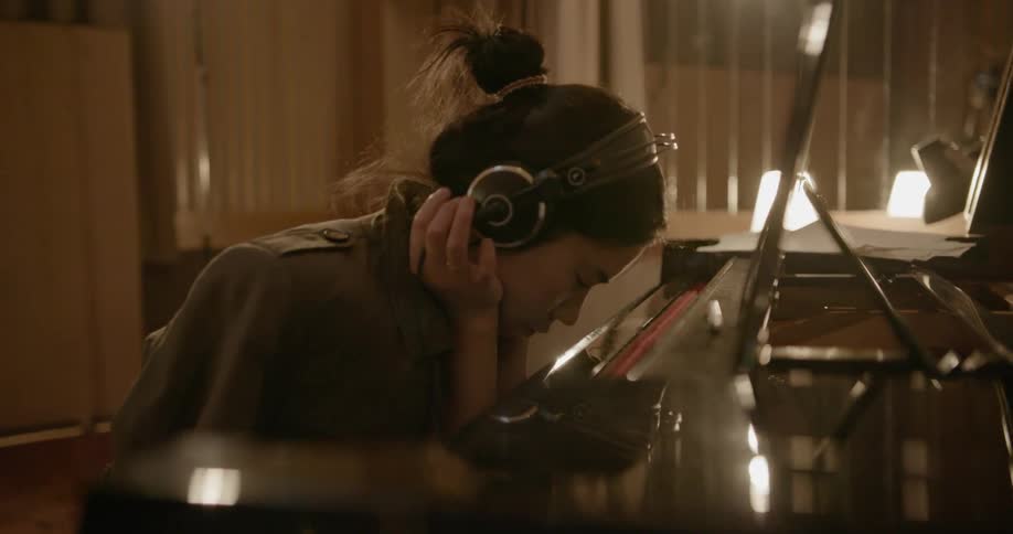 A woman is sitting at a piano in a recording studio thinking and listening