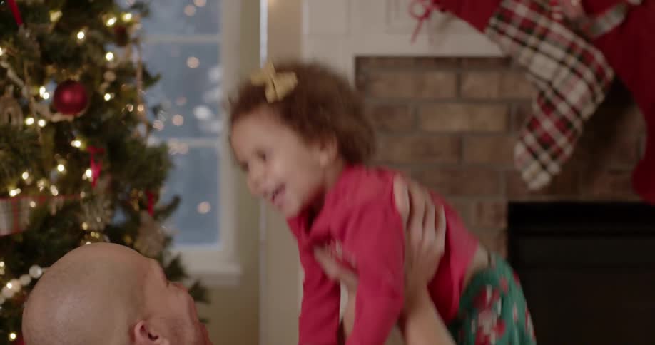 A man tosses a girl into the air next to a christmas tree