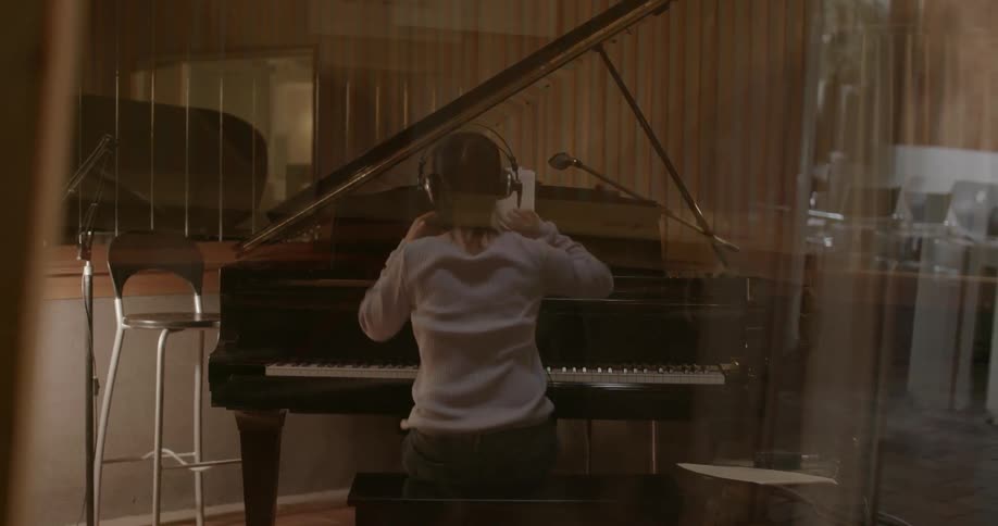 Woman sits down at a piano and puts headphones on