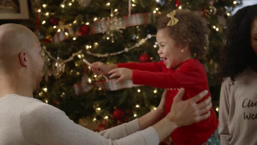 Man plays with a young girl next to a christmas tree