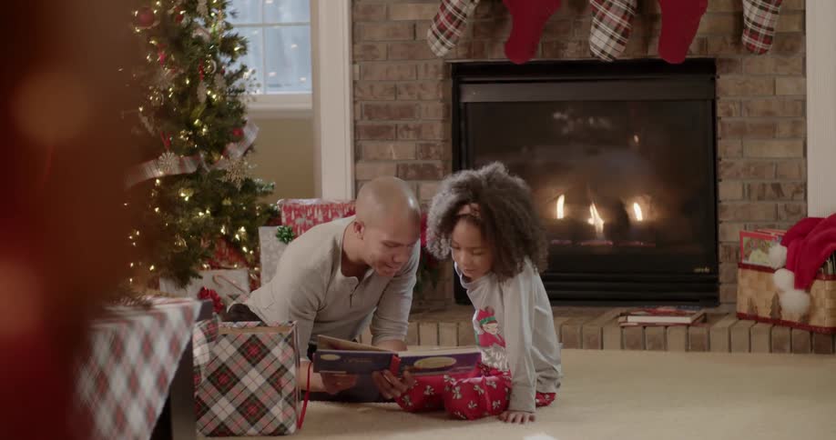 A man and girl read a book next to a christmas tree
