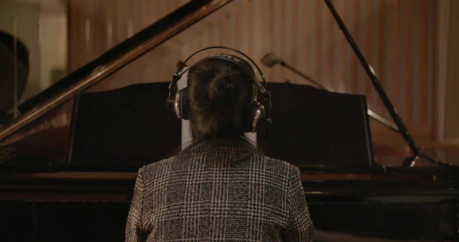 A woman wearing headphones plays the piano