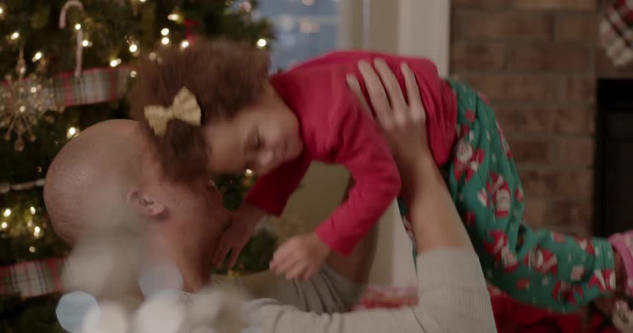 Parent lifts laughing girl in front of christmas tree