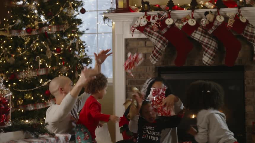 A family sitting by the fireplace throws wrapping paper into the air on christmas