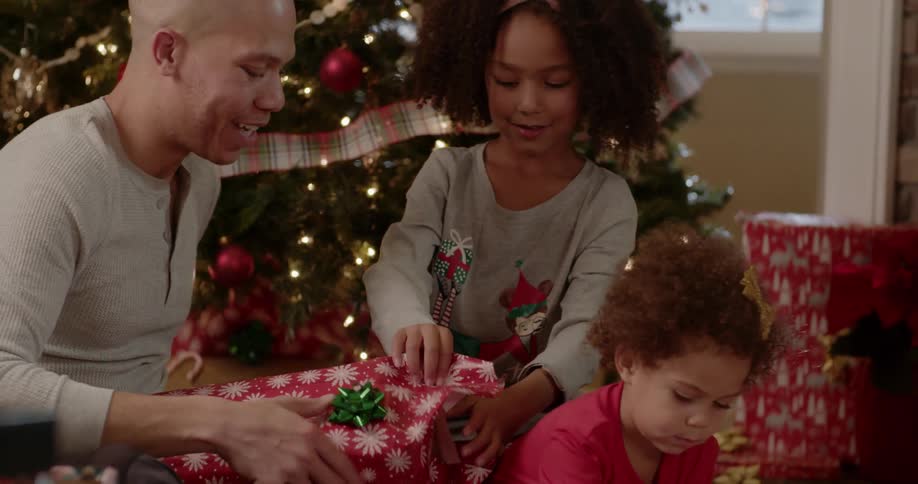 Child hugs man in front of a christmas tree