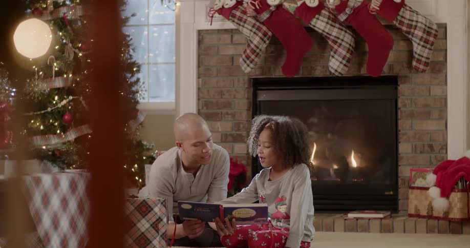 A father and daughter read next to a christmas tree