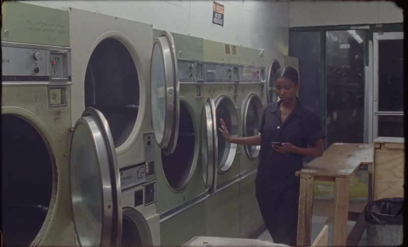 A woman is looking at her cellphone while working in a laundromat at night