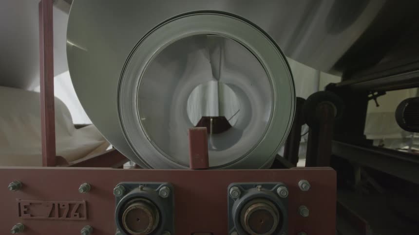 A large roller system is feeding material into a machine inside a manufacturing plant