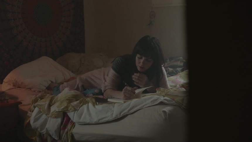 A woman lies in bed and writes in a journal