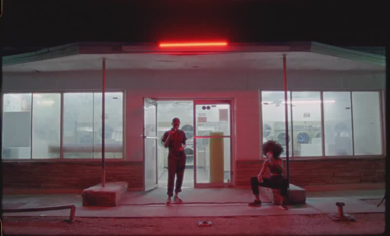 Man and woman stand and sit outside of a laundromat at night