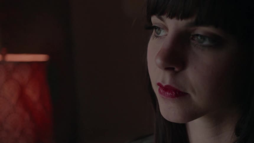 A woman sits in a dark room next to a lamp