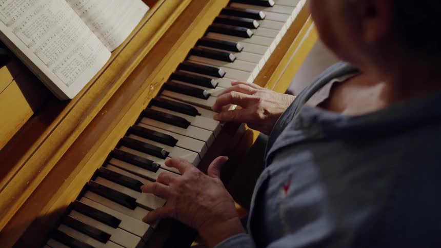 A woman wearing glasses plays the piano