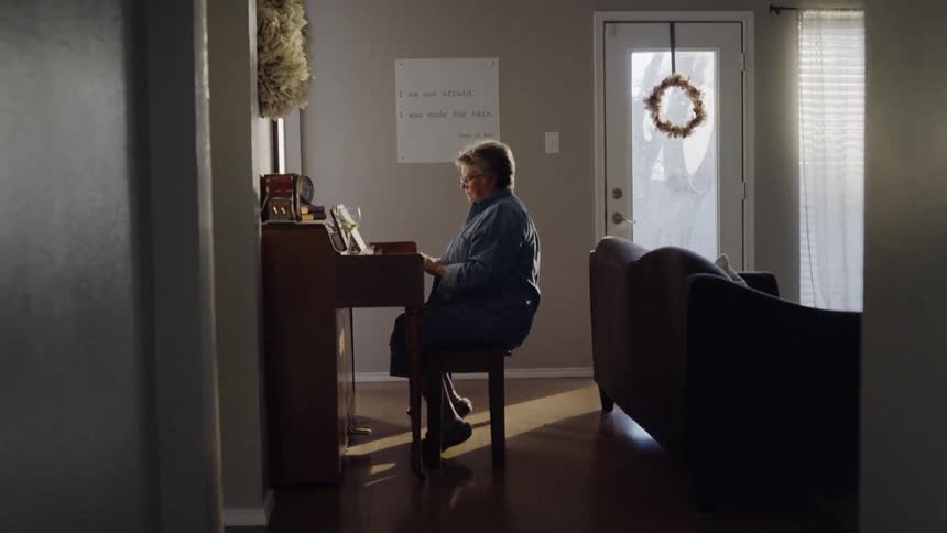 A woman wearing glasses plays the piano