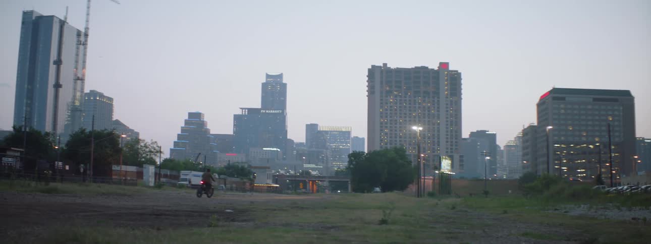 Someone is riding a dirt bike in a field with a large city in the background