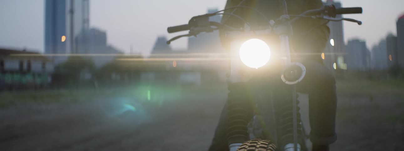 A man sits on a motorcycle with its headlight on