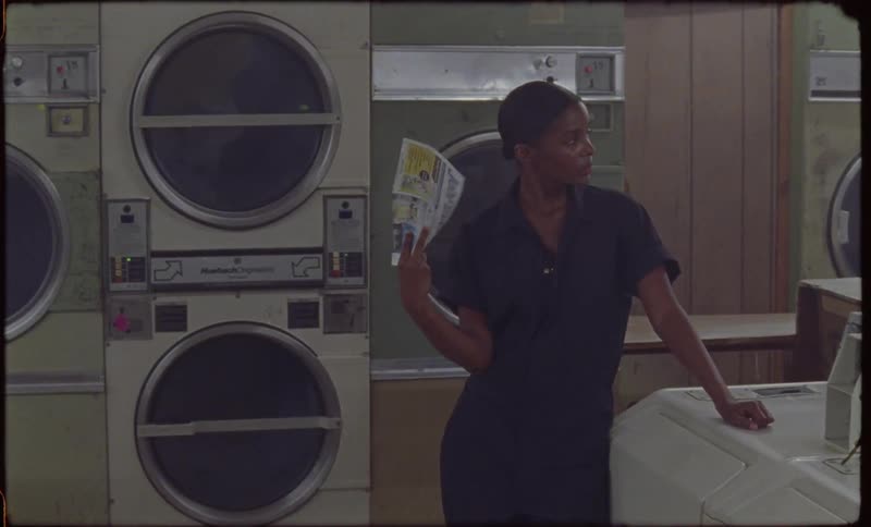 A woman is fanning herself as she stands in a laundromat