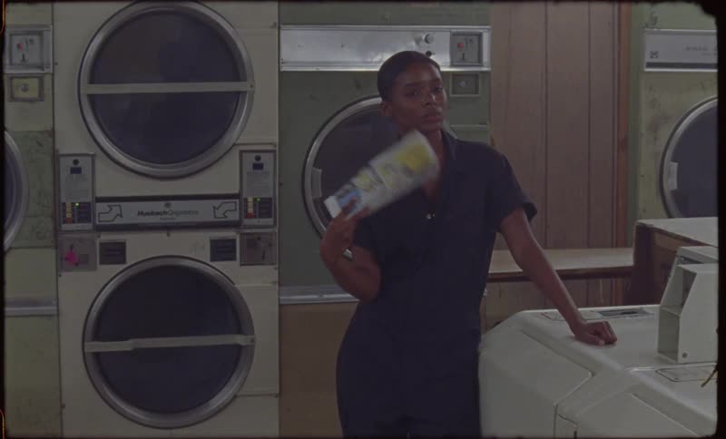 Woman stands in a laundromat fanning herself with a piece of paper