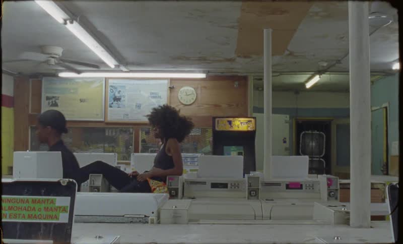A woman sits on top of a washing machine in a laundromat