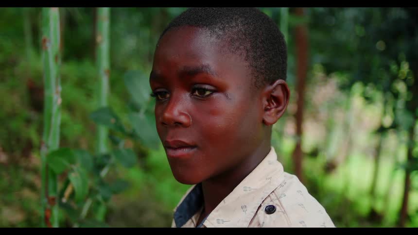 A boy is standing in a jungle during the day in deep thought