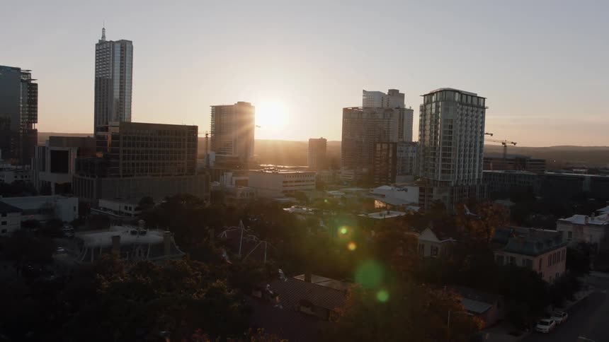 Birds fly over trees and city streets at sunset