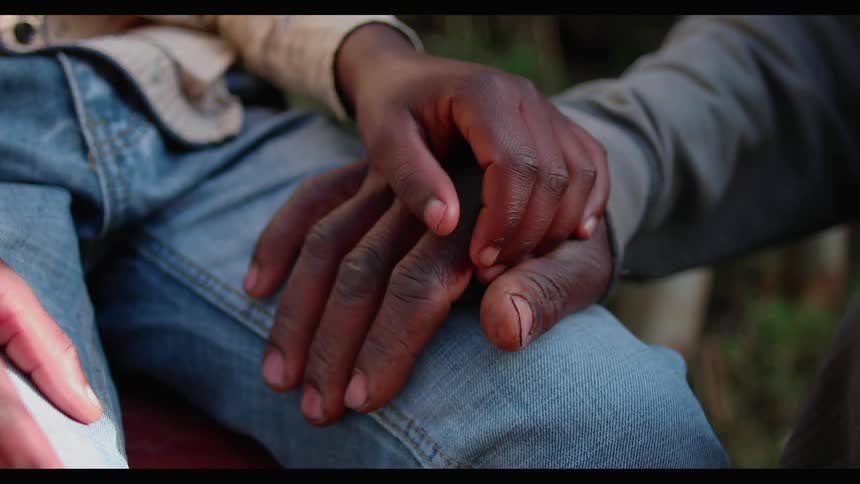 A boy is resting his hand on the hand of a man outside during the day