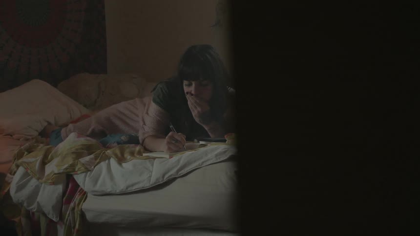 A woman lays in bed while writing in a notebook